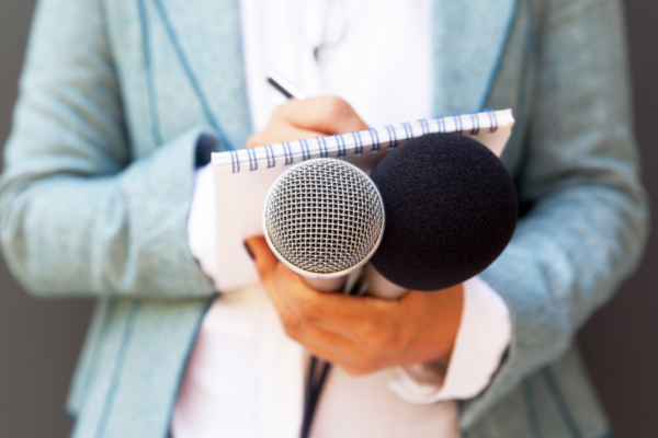 A person holds a note pad and two microphones.